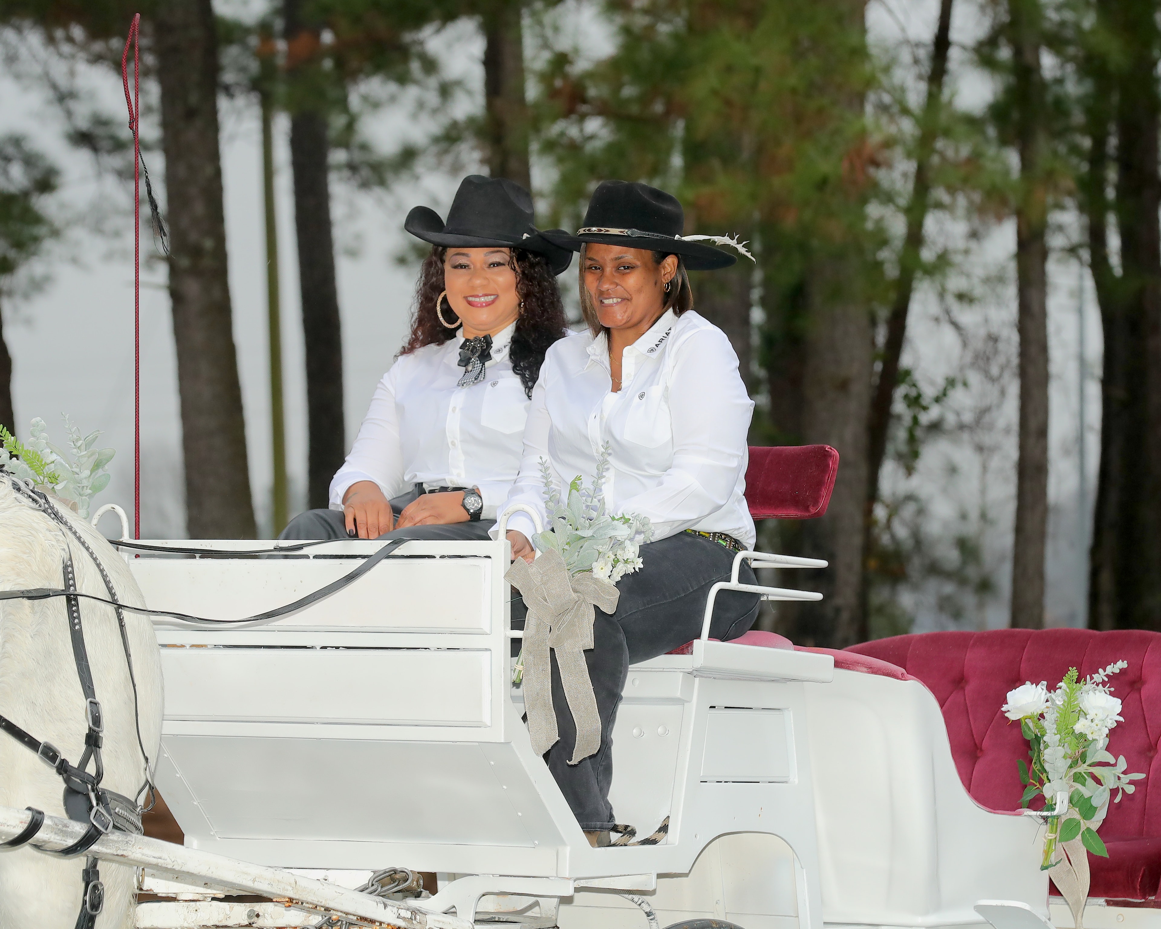 Two women in cowboy hats seated on a decorated white carriage