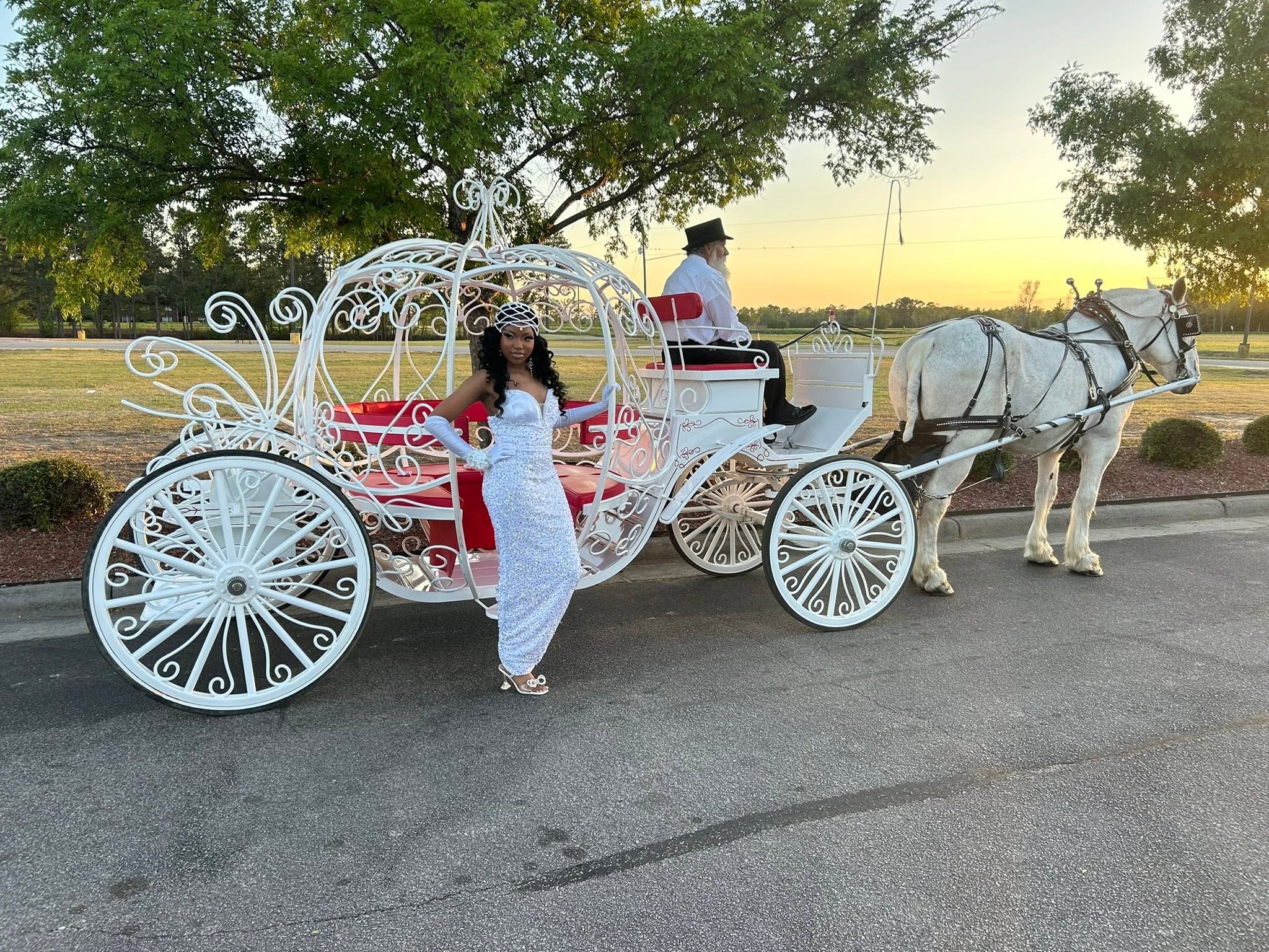 Young woman in a sparkling gown posing beside the Cinderella carriage at sunset
