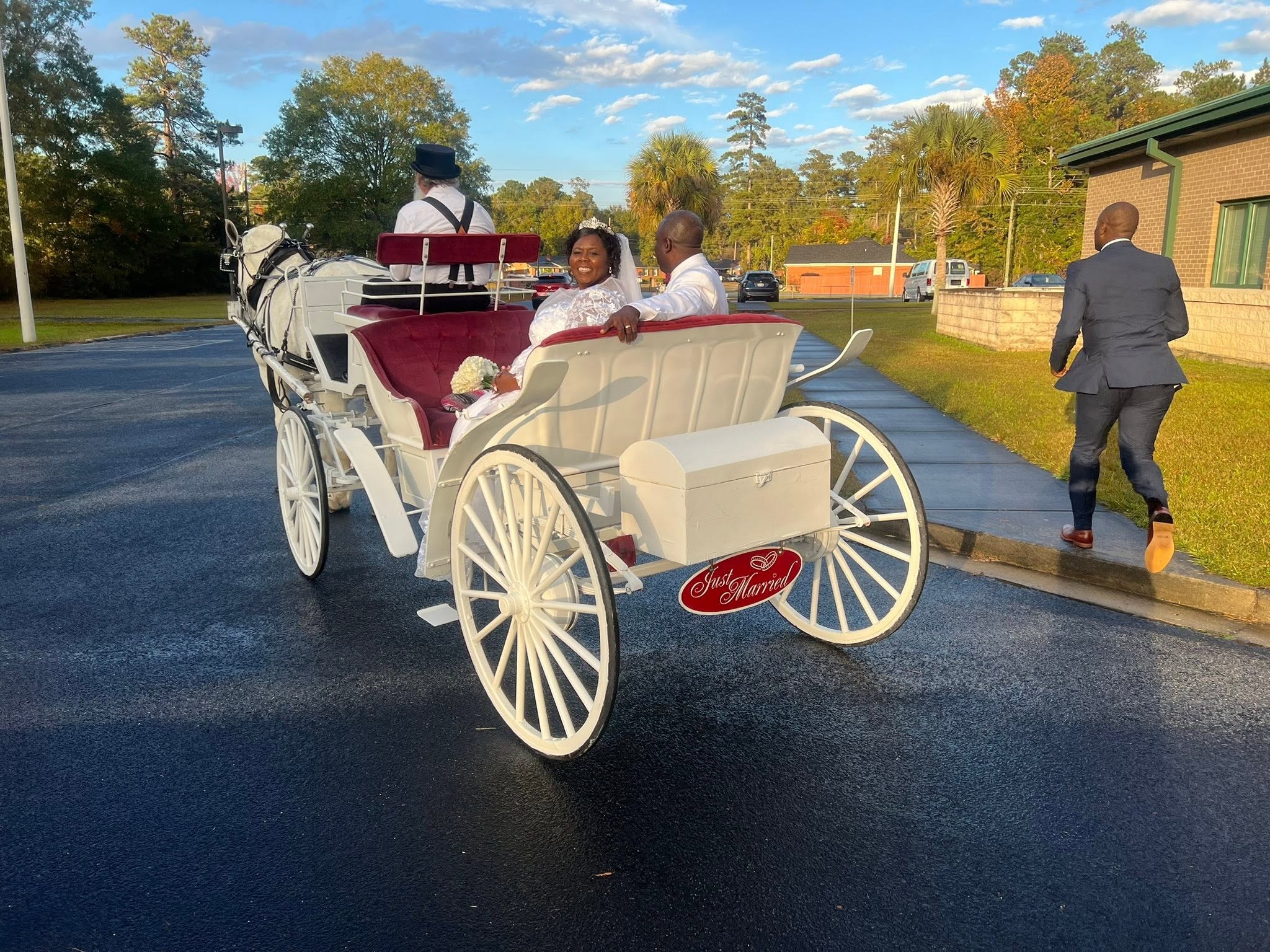 Bride and groom smiling in a white Just Married horse-drawn carriage